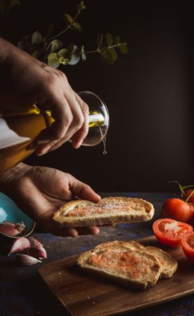 Crop person pouring oil on toasts