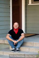 Man with red bandana around his neck sitting on steps in front of house smiling 5wXE94