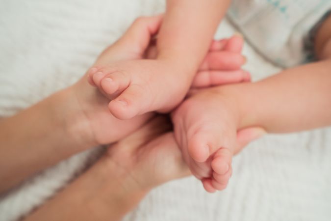 Hands holding legs of little baby on bed