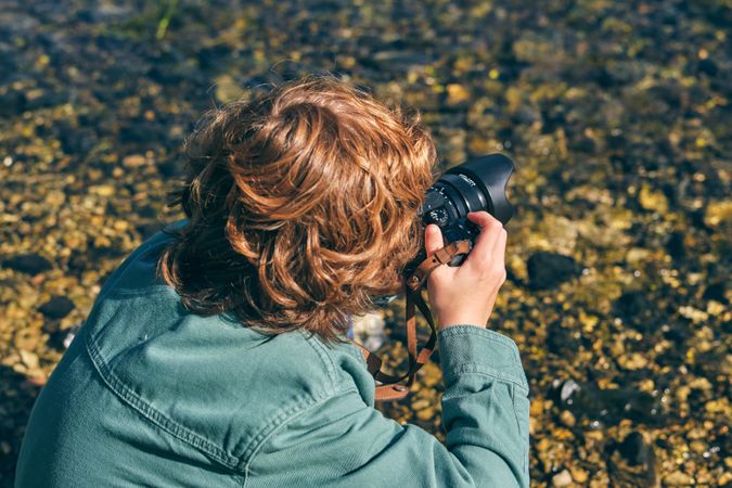Faceless boy photographing river on shore