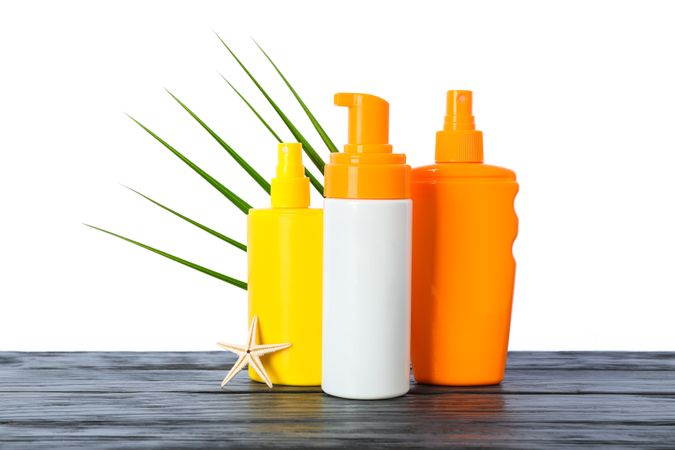 Sunscreen sprays with starfish and palm leaf on wooden table isolated on studio background. Safe tan accessories
