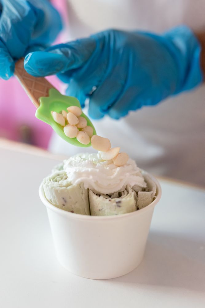 A worker is decorating a rolled ice cream tub with yogurt bubble toppings with a spoon