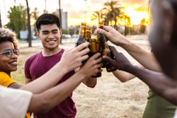 Happy multi-ethnic friends and clinking their beer bottles together outside