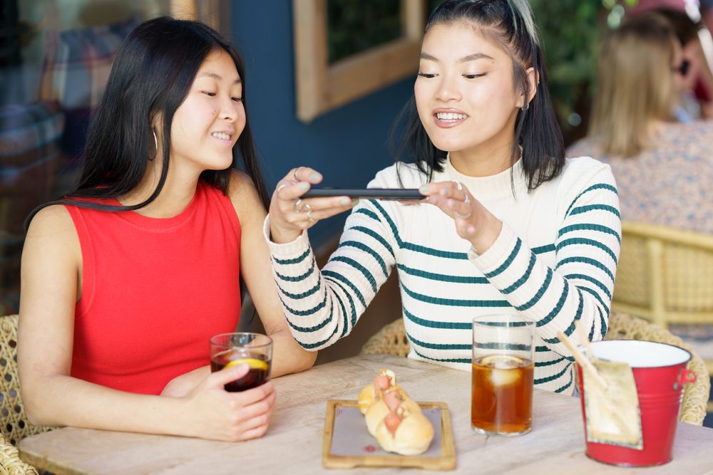 Two women sitting in restaurant patio using their phone to take picture of their meal
