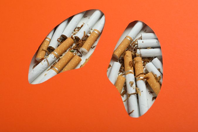 Close up of lung shape cut out of orange paper with cigarettes