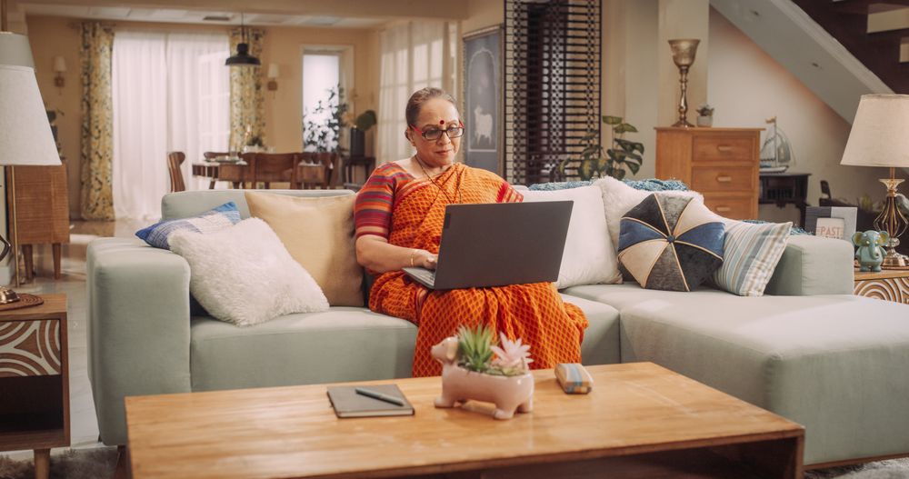 Older Indian Woman Using Laptop at Home: Immersed in Captivating Online Stories, Exploring New Ideas