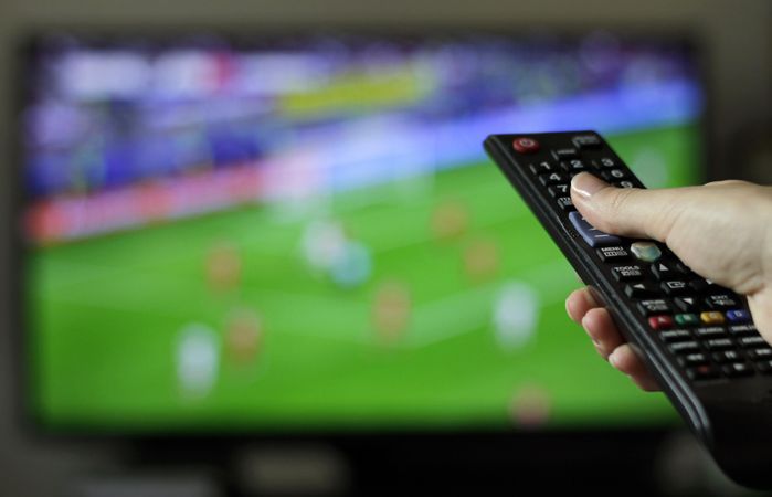 Cropped image of hand holding remote control during a football match on TV