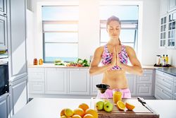 Woman in prayer stance with hands together in kitchen over breadboard with fresh fruit and juice