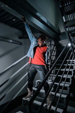 Black person putting on jeans jacket on staircase