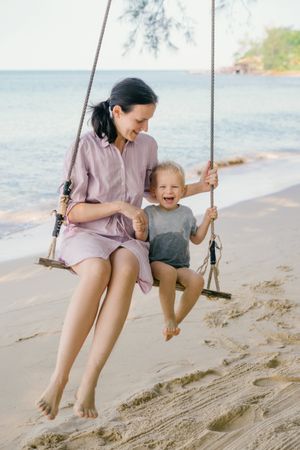 Joyful kid swinging with mother against blurred seascape