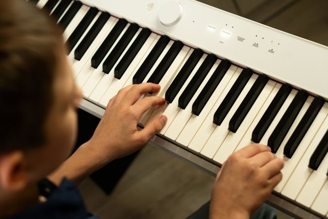 Overhead view boy's hands pressing piano keys on digital keyboard.