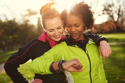 Two women checking a smart watch in a sunny park