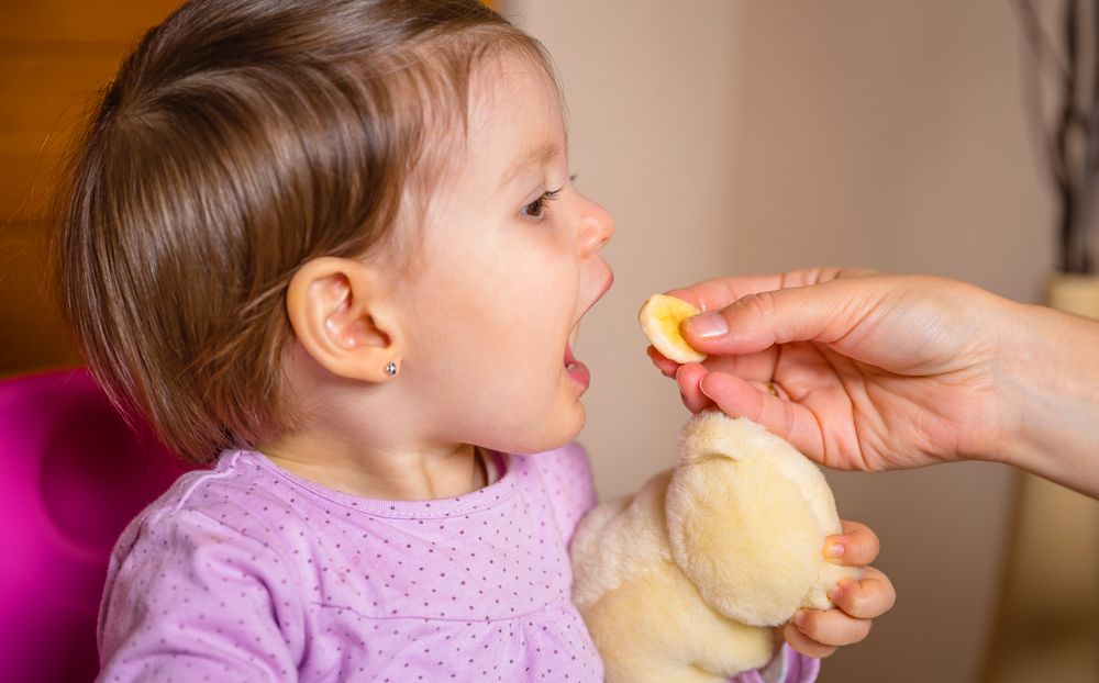 Baby eating banana slice from the hand of mother