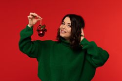 Smiling woman in green sweater holding red Christmas ornament.