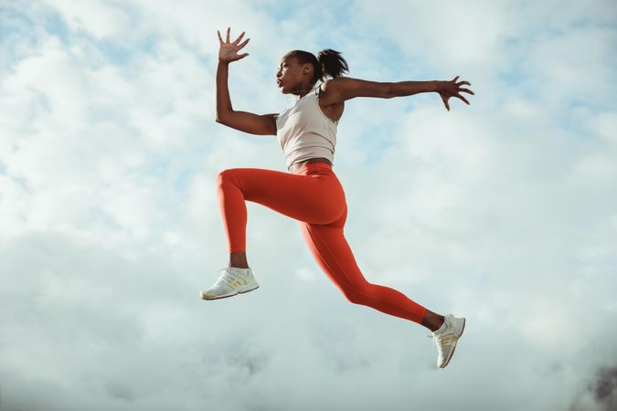Fitness woman running and jumping in midair against sky