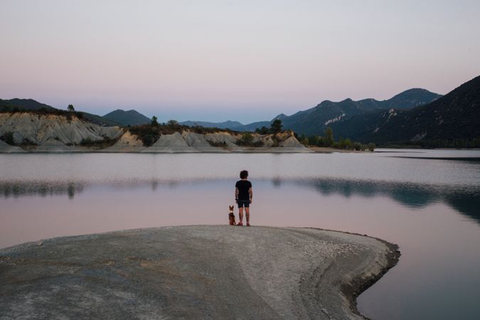 Male trekker and his dog standing on the edge of a lake