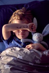 Boy covering eyes with hand while lying in bed