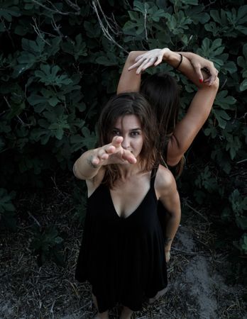 Young women posing near green bush