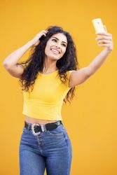 Female in yellow t-shirt taking selfie in front of mustard background