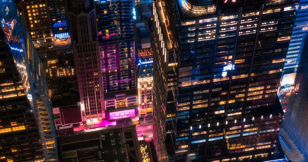 Helicopter Tour of New York Cityscape at Night. Manhattan Offices with Lights and Congested Streets with Cars and Taxi Vehicles in a Big City. Building with Pink Neon Billboard