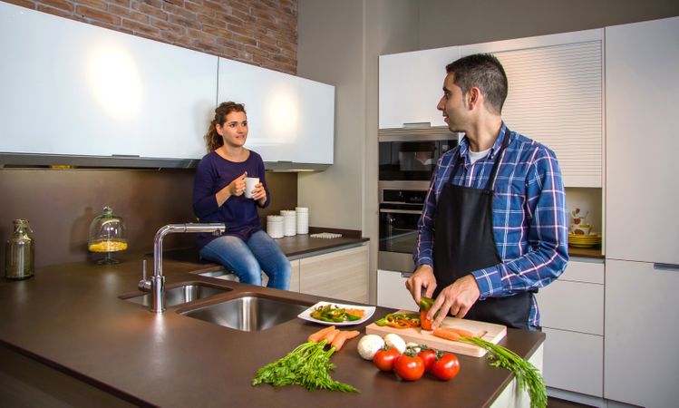 Couple talking in the kitchen while the husband cuts vegetables to prepare food
