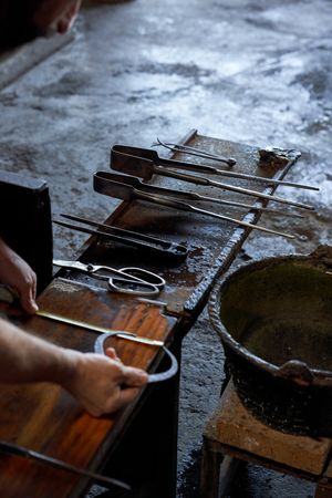 Hands of glassblower with tools making glass in workshop