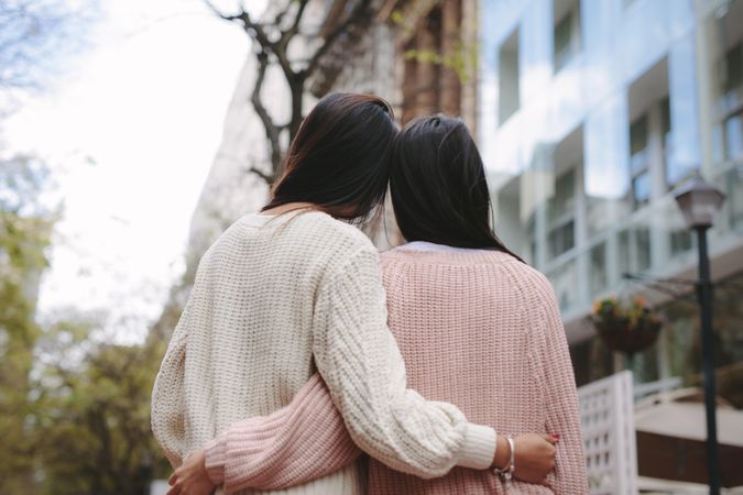 Two young women hugging in sweaters shot from behind