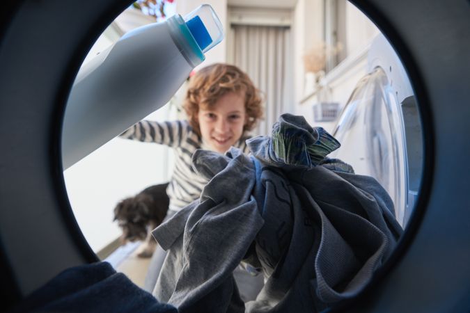 Smiling child with detergent loading clothes in washing machine