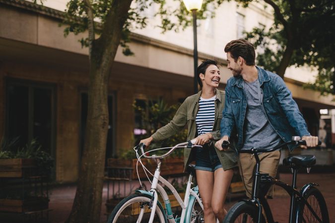 Happy man and woman walking on a street with their bikes