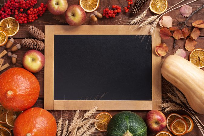 Squash, dried orange, apples and cinnamon sticks surrounding a board