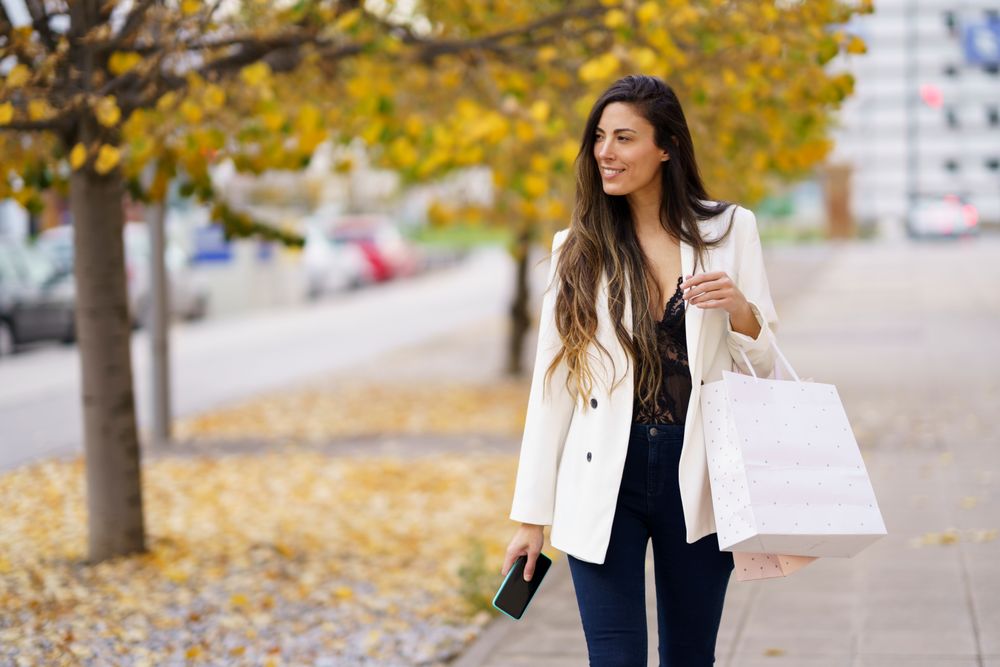 A fashionable woman joyfully shops among colorful autumn leaves using her smartphone