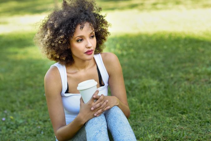 Black woman with afro hairstyle gazing while sitting in park with a coffee