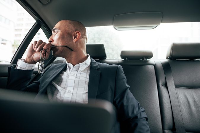 Man holding eyeglasses sitting in his sedan on back seat