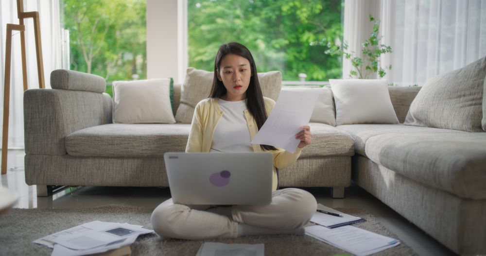 South Korean Woman Sitting on a Floor, Working on Her Project on a Laptop Computer in a Stylish Bright Living Room