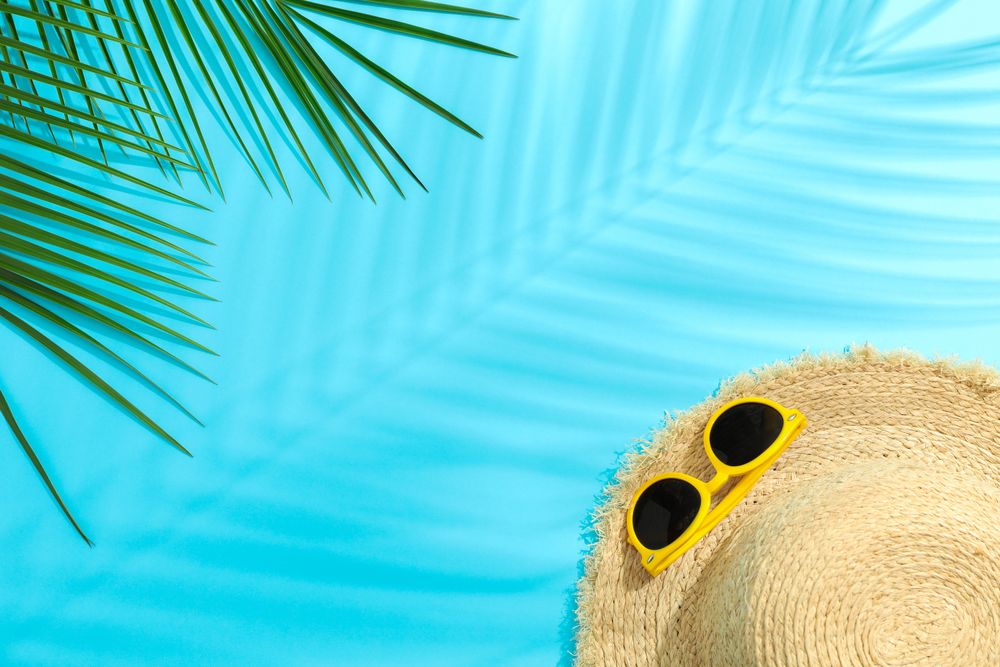 Palm leaves, straw hat and sunglasses on color background, space for text. Summer vacation backdrop