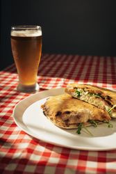 Gourmet pizza in open box with herbs, cheese, prosciutto, tomato, and pesto