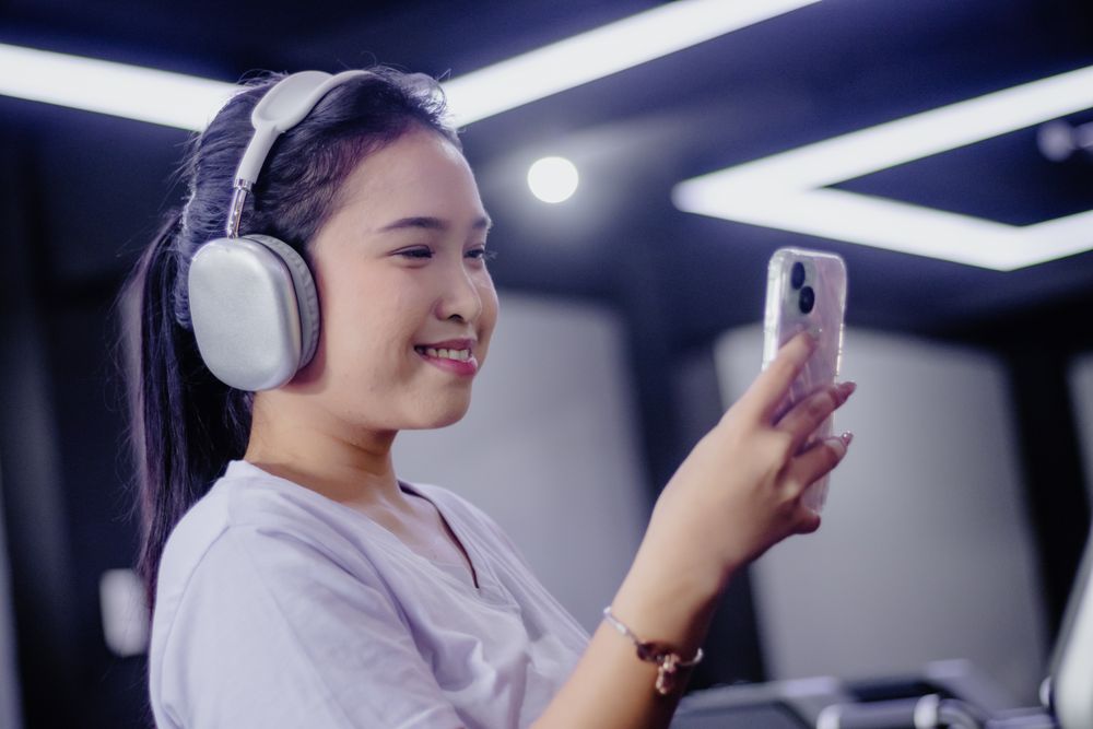 Smiling Asian Woman Enjoys Music with Headphones and Mobile Phon