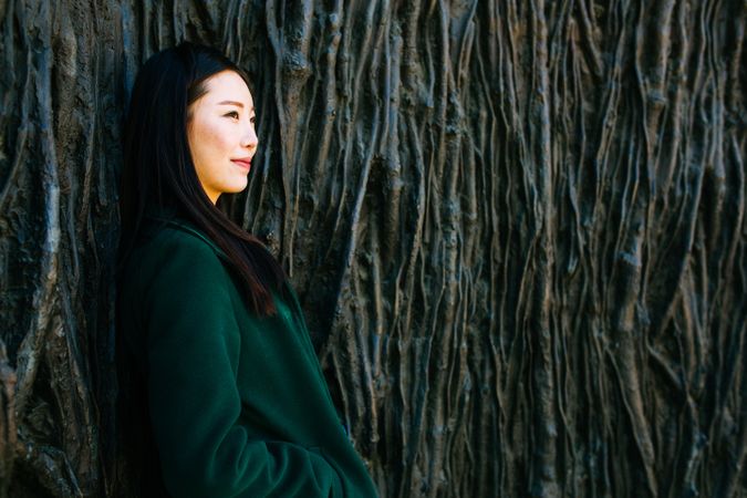 Pensive Asian woman leaning on rough wall