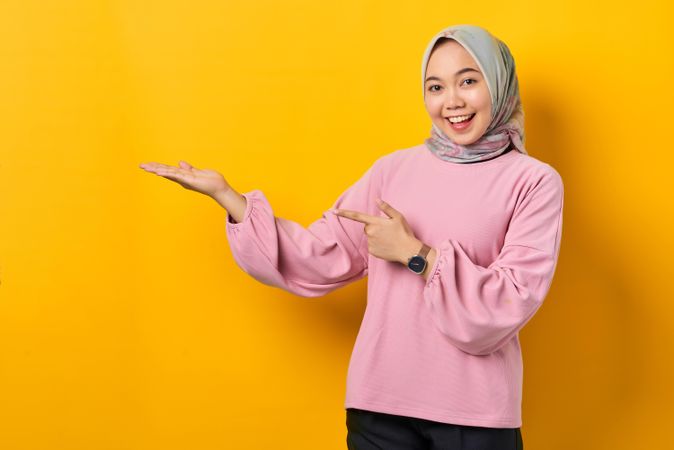 Happy Muslim woman in scarf and pink sweater presenting copy space studio shoot