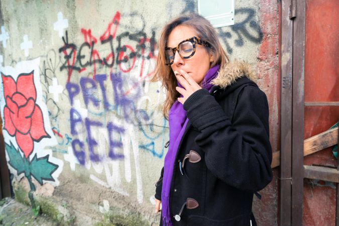 Woman in glasses smoking next to grafitti