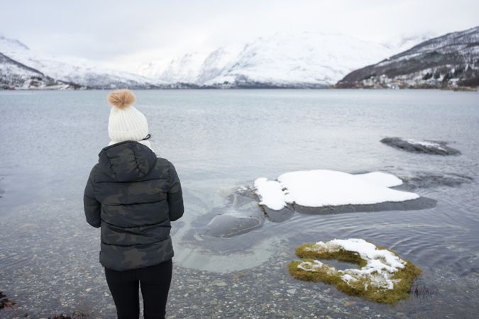 Anonymous person on pond shore against highland in winter