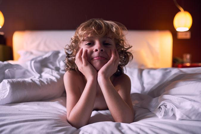 Funny little boy lying on soft bed