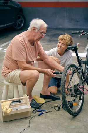 Mature man repairing bicycle with screwdriver near grandson