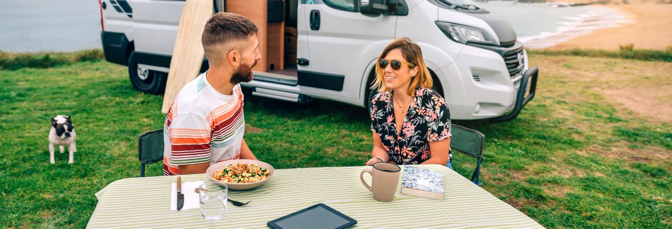 Male and female sitting at table outside parked motorhome