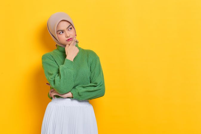 Woman in headscarf pondering something with hand on her chin with copy space