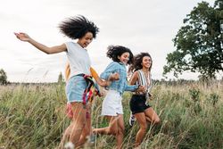 Four women holding hands running on field