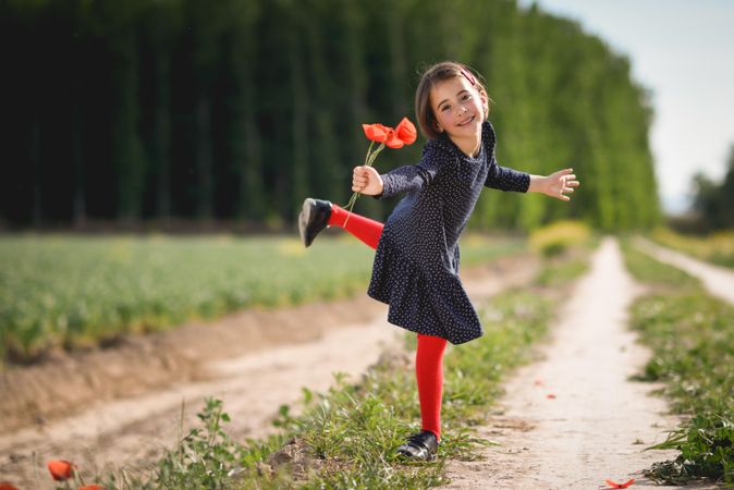Smiling girl balancing on one leg with red flowers in her hand