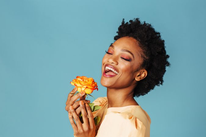Studio shot of a joyful Black woman with a yellow rose and her eyes closed
