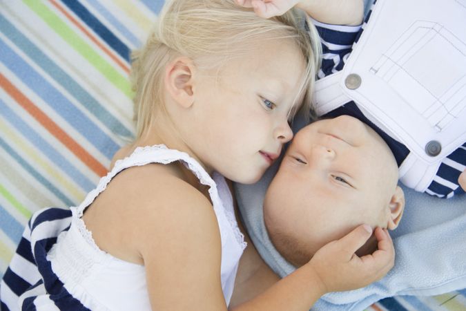Little Sister Laying Next to Her Baby Brother on Blanket