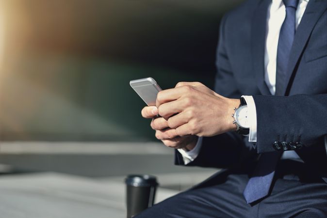 Man in business attire holding cell phone with to-go coffee